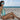 Woman with glowing, bronzed skin wearing a turquoise swimsuit and sunglasses on a sandy beach.